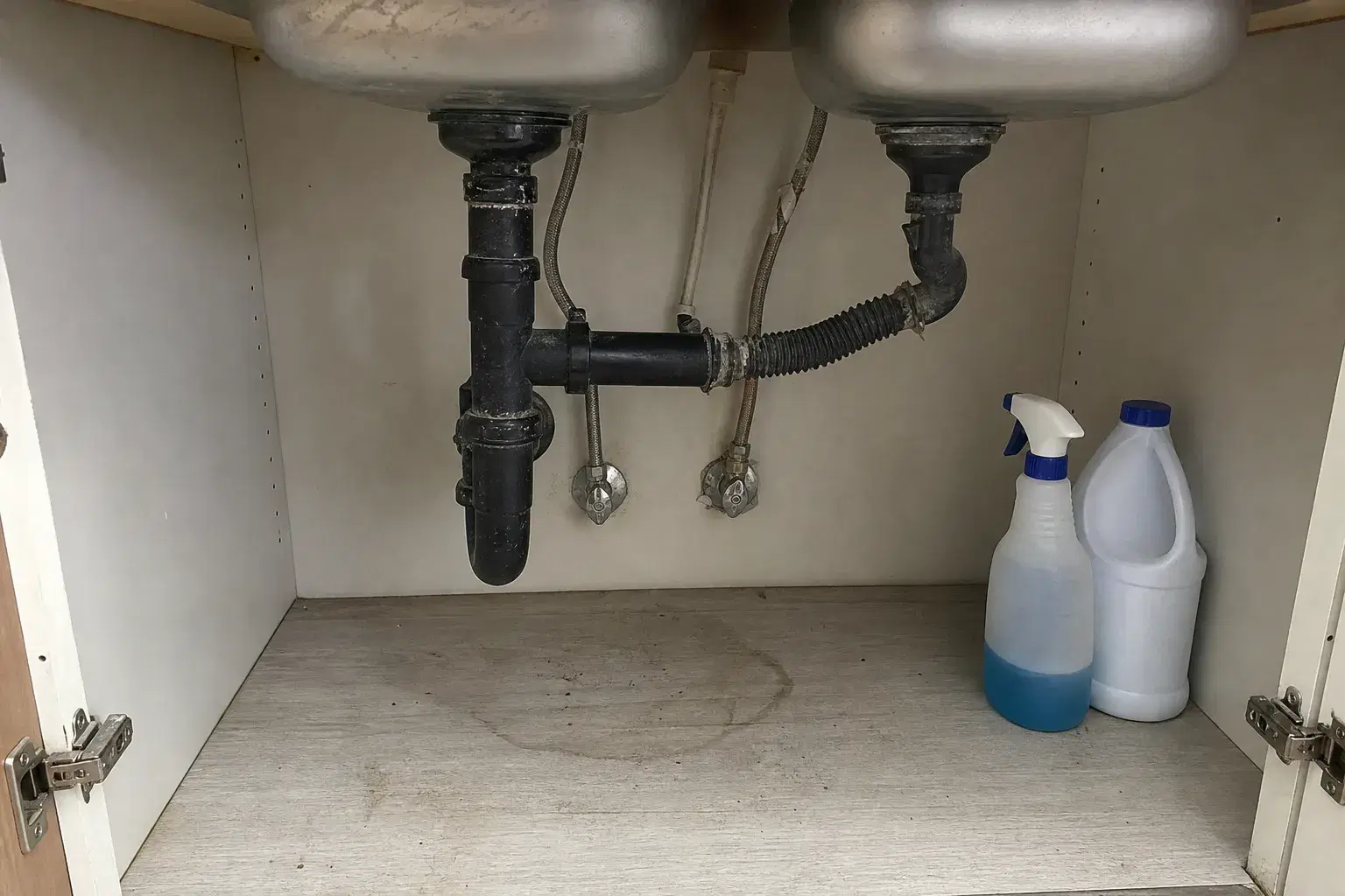 Kitchen sink cabinet with visible plumbing issue and supplies before a handyman repair