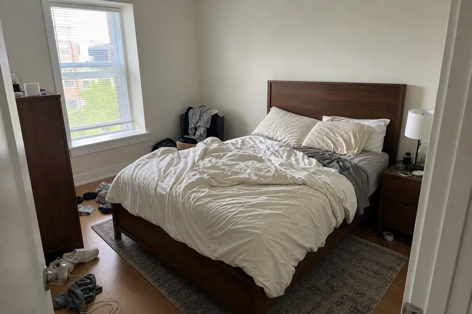 Apartment bedroom with an unmade bed, loose clothes, and everyday clutter before cleaning